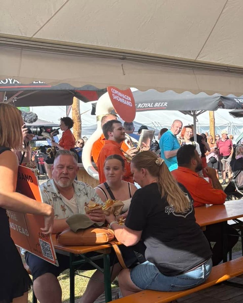 Gæster spiser burgere og pommes frites ved bordene i et festivaltelt